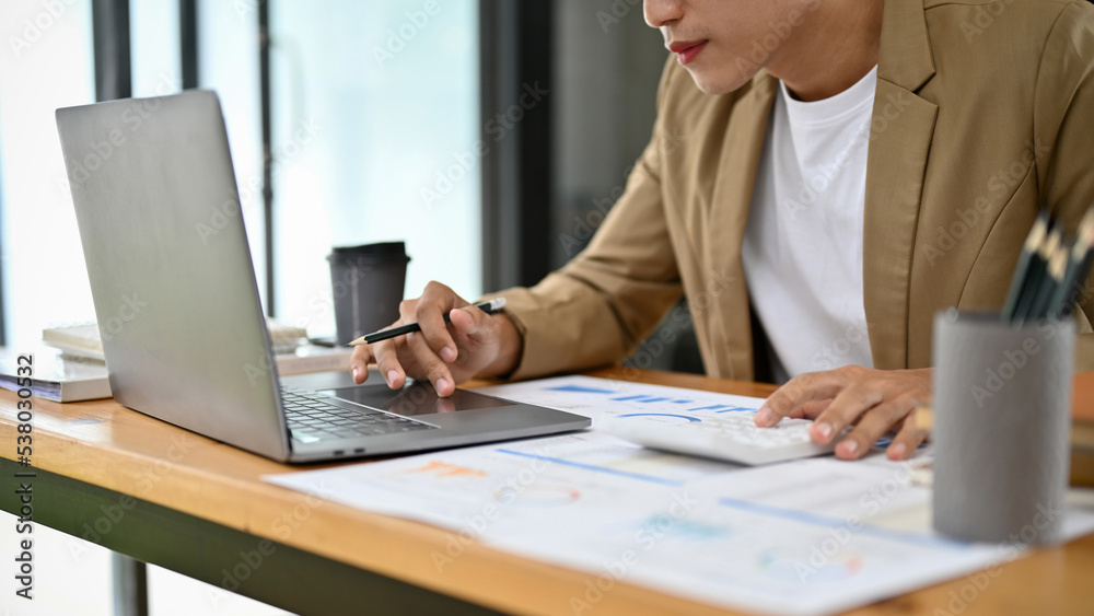 Smart and handsome Asian businessman using laptop and working on his financial paperwork. Smart and handsome Asian businessman using laptop and working on his financial paperwork.