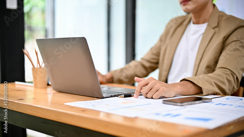 Professional Asian male boss working at his desk, using laptop and examining financial report