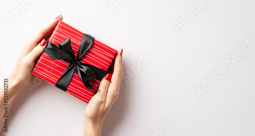 Black friday shopping concept. First person top view photo of young woman's hands giving red giftbox with black bow on isolated white background with copyspace © ActionGP