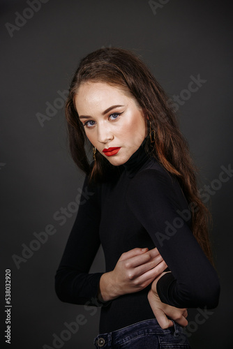 A model in bright make-up in a black sweater against the background of a dark wall