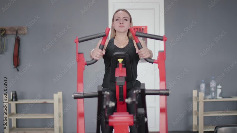 Front view of blonde woman trains on red training apparatus in gym. Front view of blonde woman trains on red training apparatus in gym.