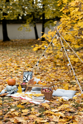 Cozy composition of autumn picnic outdoors. Rustic decor with ripe red apple in wooden basket, pumpkin, plaid, delicious food, books. Fall vibes