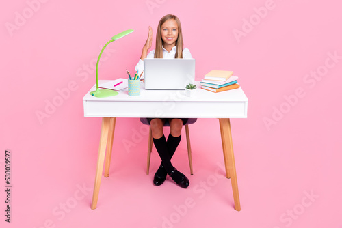 Full size photo of intelligent smart schoolgirl blond hair school uniform sit on desk raise hand isolated on pink color background