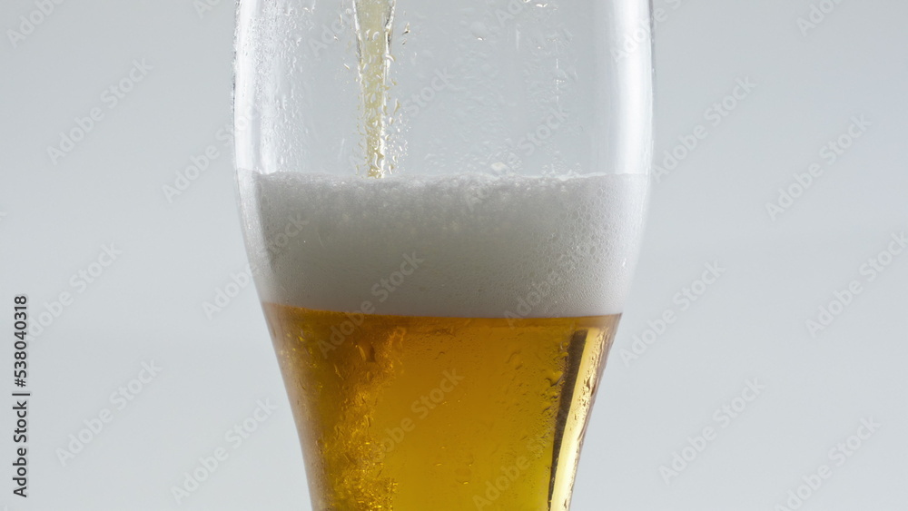 Closeup beer pouring glass making tasty dense foam at white background. Closeup beer pouring glass making tasty dense foam at white background.