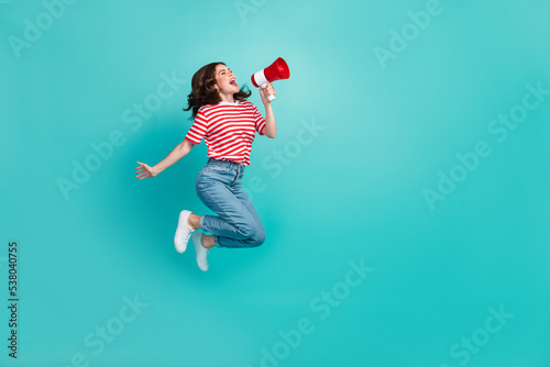 Full length photo of pretty cute girl dressed red t-shirt jumping high shouting bullhorn empty space isolated teal color background photo