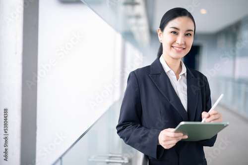 Young Asian business woman holding a tablet looking away, Fashion business photo of beautiful girl in casual suite with tablet .
