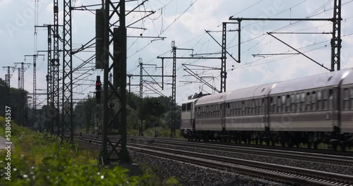 a european passenger train passing through in germany on a summer day at the countryside disappearing in the distance getting out of focus plants and masts around lights in background 4K Film 50 fps