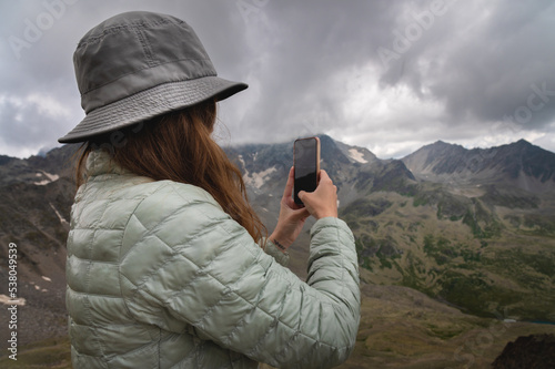 woman takes a picture on the phone while standing on top of a hill. Portrait of a tourist in the mountains