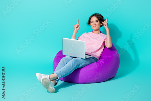 Full length photo of pretty girl brown hair pink t-shirt jeans sit on bean bag indicating empty space isolated on teal color background