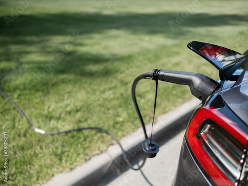 Black electric car charging outdoors in summer.