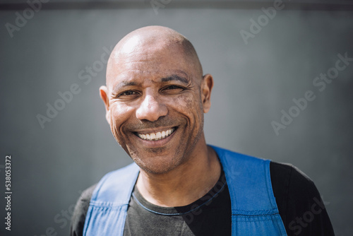 Portrait of happy bald construction worker against wall