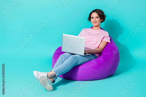 Photo of adorable lady pink outfit jeans sit cozy chair use device enjoy distance remote work empty space isolated on cyan color background