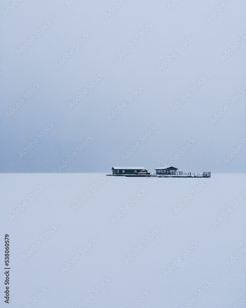 Naklejka premium Vertical shot of buildings in the middle of a plain snow field under a very cloudy sky