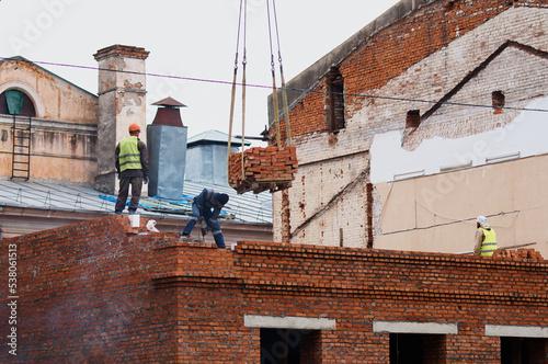 Workers building a red brick house. Reconstruction of part of a historic building. Walls, windows, the roof of an old building in the background