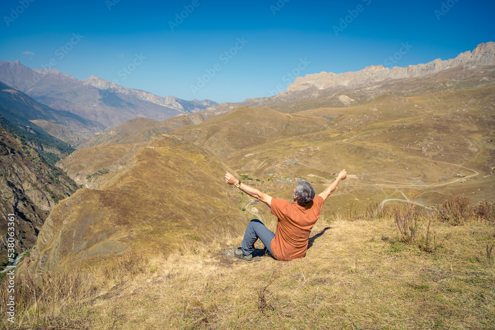 A man in the mountains with open arms looks into the distance, enjoying the scenery of the mountains.