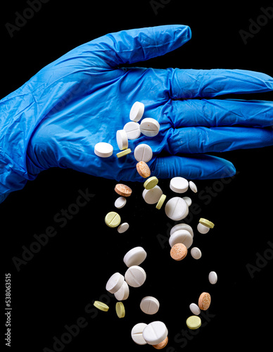 Medical pills on an isolated black background with reflection dropped from hand
