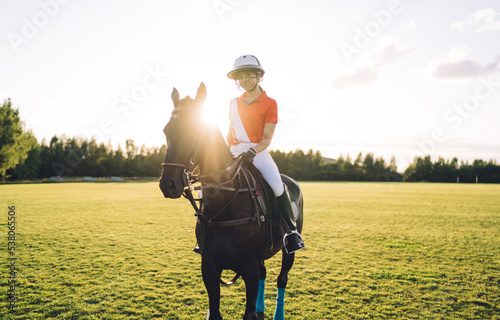 Young woman in polo uniform on horseback on playing field