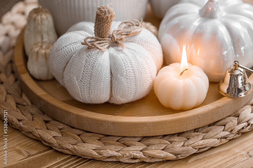 Still-life. Knitted pumpkin,  pumpkin-shaped candles and white ceramic pumpkins on a wooden tray on a coffee table in the home interior of the living room. Cozy autumn concept.