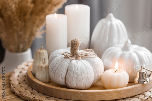 Still-life. Knitted pumpkin, pampas grass, pumpkin-shaped candles and white ceramic pumpkins on a wooden tray on a coffee table in the home interior of the living room. Cozy autumn concept.