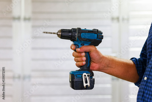 Close up a handy man hands hold electric hammer drill in workshop, copy space. 