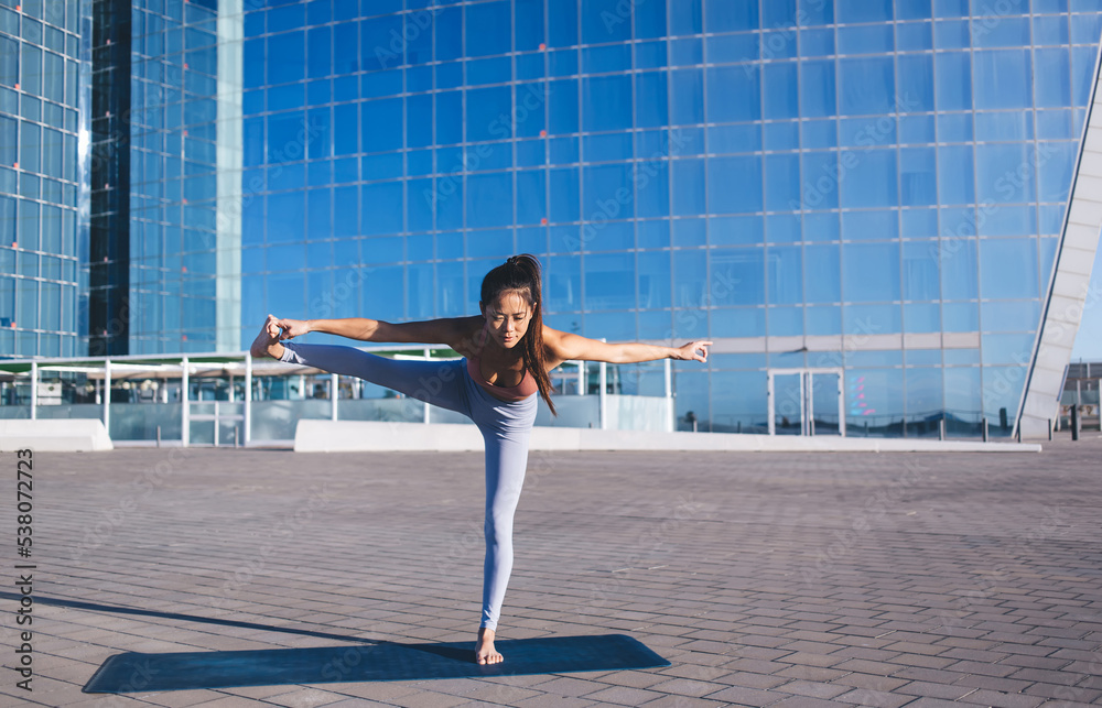 Experienced young woman standing on one leg and stretching another during yoga for develop flexibility and achieve harmony of body, Asian fit girl engaged in meditation practice healthy lifestyle