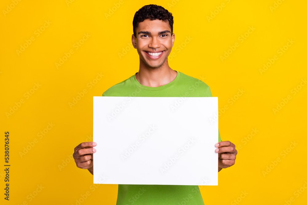 Photo of young attractive handsome smiling guy hold white paper billboard recommend advertisement placard isolated on yellow color background Photo of young attractive handsome smiling guy hold white paper billboard recommend advertisement placard isolated on yellow color background