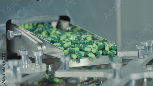 Green capsules move along the metal automatic conveyor, fall into the drum for sorting and preparation for packaging. Medicine production line in pharmaceutical factory. Pharma company