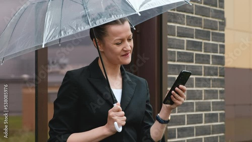 A woman in a black jacket under a transparent umbrella, on the street of the city, outdoors. Rain.