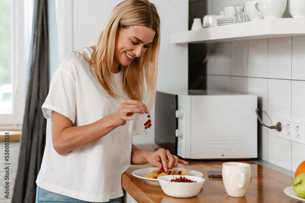 Happy woman laughing and holding berries while making breakfast at home