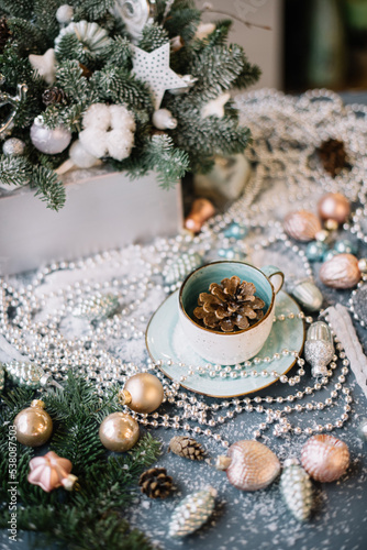 Beautiful festive winter set: pine cone in a cup, ornaments, beads, spruce branches, fake snow, glitter on the grey table background, close up view 