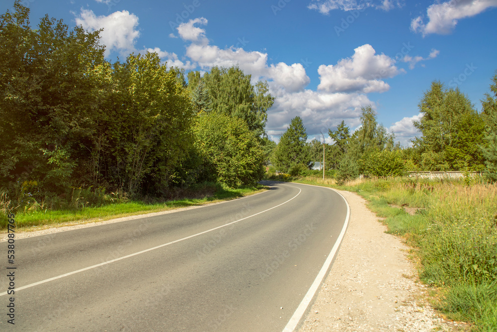 Close-up of a small empty highway in the countryside. Road turning between trees. Suburban asphalt two-lane road. Close-up of a small empty highway in the countryside. Road turning between trees. Suburban asphalt two-lane road.
