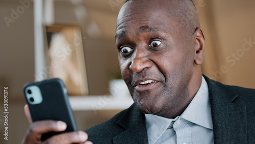 African American old 50s surprised amazed shocked man looking at mobile phone screen reading unbelievable news waving head no disagreement negation refusal shock fear amazing online sms shock reaction