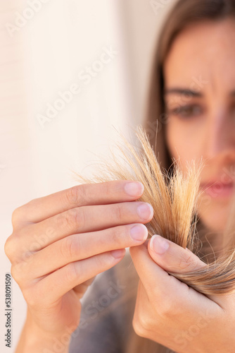 Vertical close up view of frustated cropped young woman looking and touching her blond damage hair selective focus