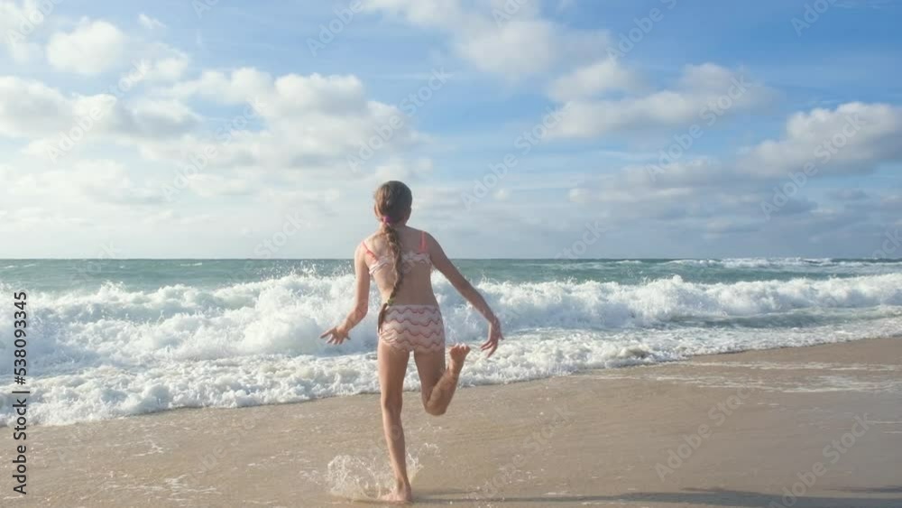 A Happy teenage girl with long hair runing along the coast of the Atlantic Ocean and jumping high. Full HD slow motion video of a child playing on the beach.