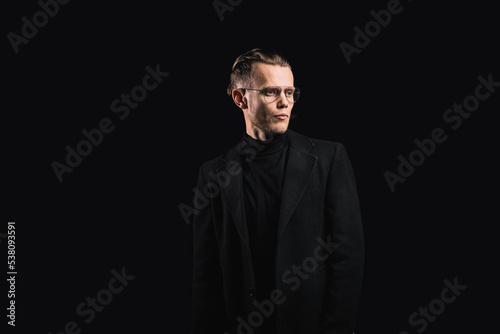 brutal young man in glasses in a black coat on a dark background, hair styling by a handsome man.