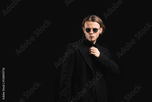 stylish man in sunglasses and a black coat on a black background, a handsome and brutal man with long hair.