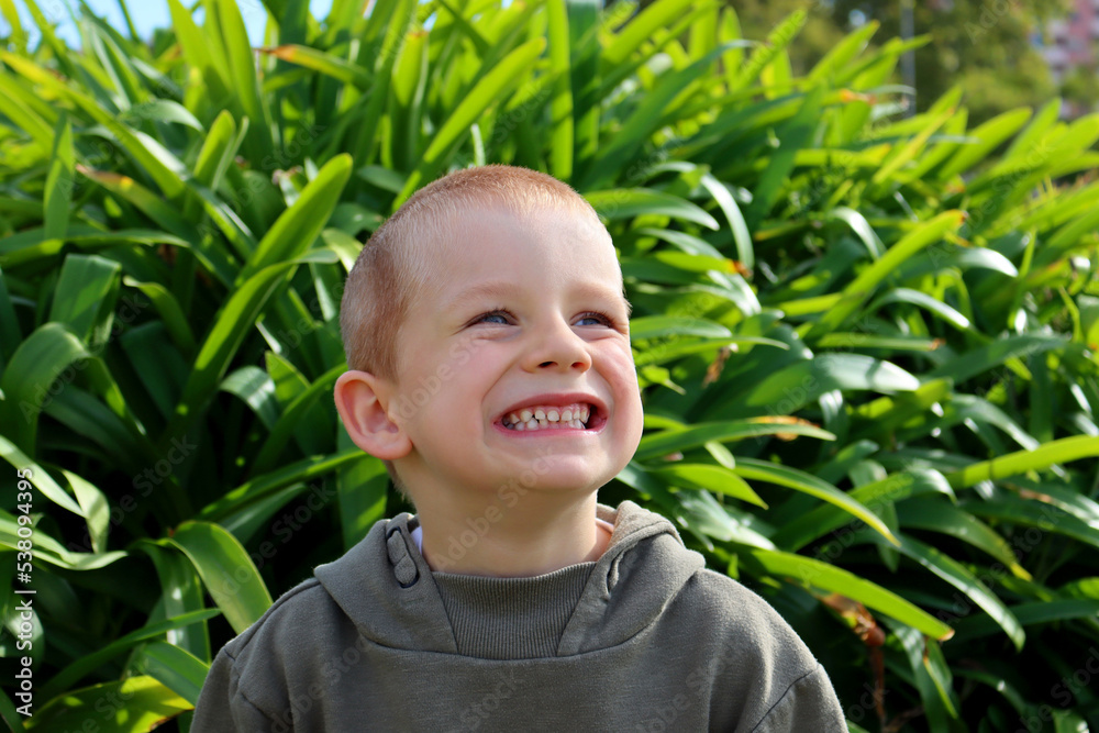 The short-haired, blond boy looks up and smiles, showing all his teeth. A five-year-old boy with a grin on his face. The short-haired, blond boy looks up and smiles, showing all his teeth. A five-year-old boy with a grin on his face.