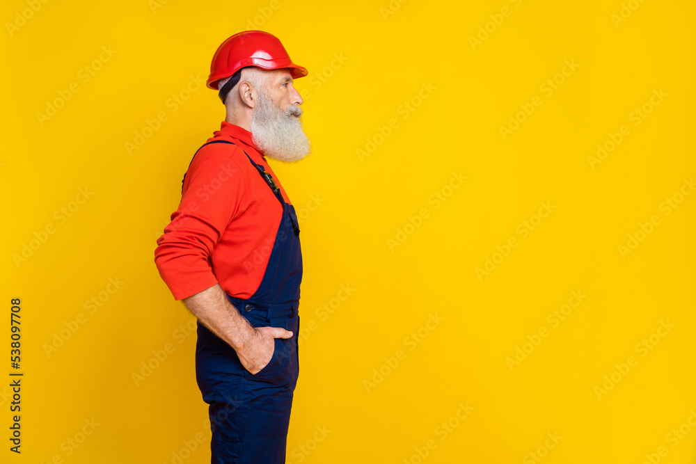 Photo of confident handsome age man workwear overall red hard hat hands arms pockets looking empty space isolated yellow color background