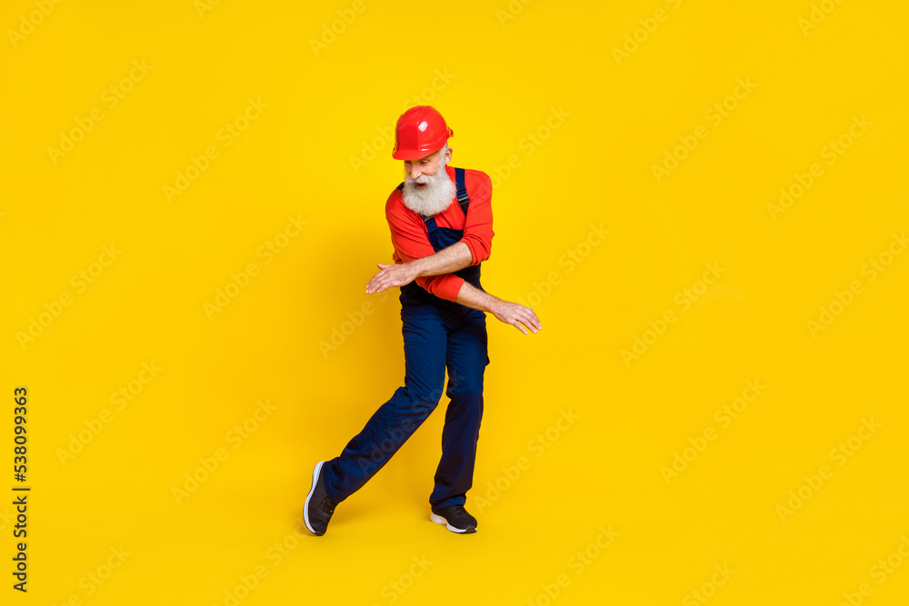 Photo of good mood cool senior guy dressed uniform overall red hardhat having fun dancing isolated yellow color background Photo of good mood cool senior guy dressed uniform overall red hardhat having fun dancing isolated yellow color background