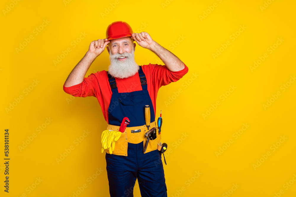 Photo portrait of handsome grandparent arms touch helmet toolbelt maintenance dressed safety uniform isolated on yellow color background