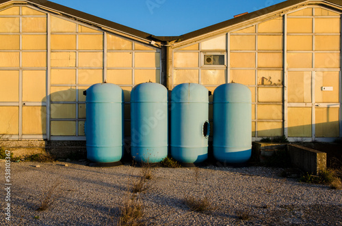 Quattro contenitori agricoli azzurri in una fattoria abbandonata illuminati dalla luce del tramonto photo
