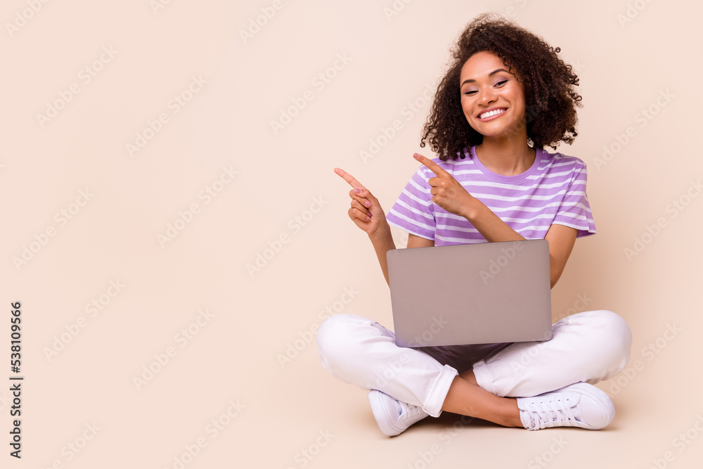 Portrait of positive gorgeous nice girl with perming coiffure laptop on legs directing empty space isolated on beige color background Portrait of positive gorgeous nice girl with perming coiffure laptop on legs directing empty space isolated on beige color background