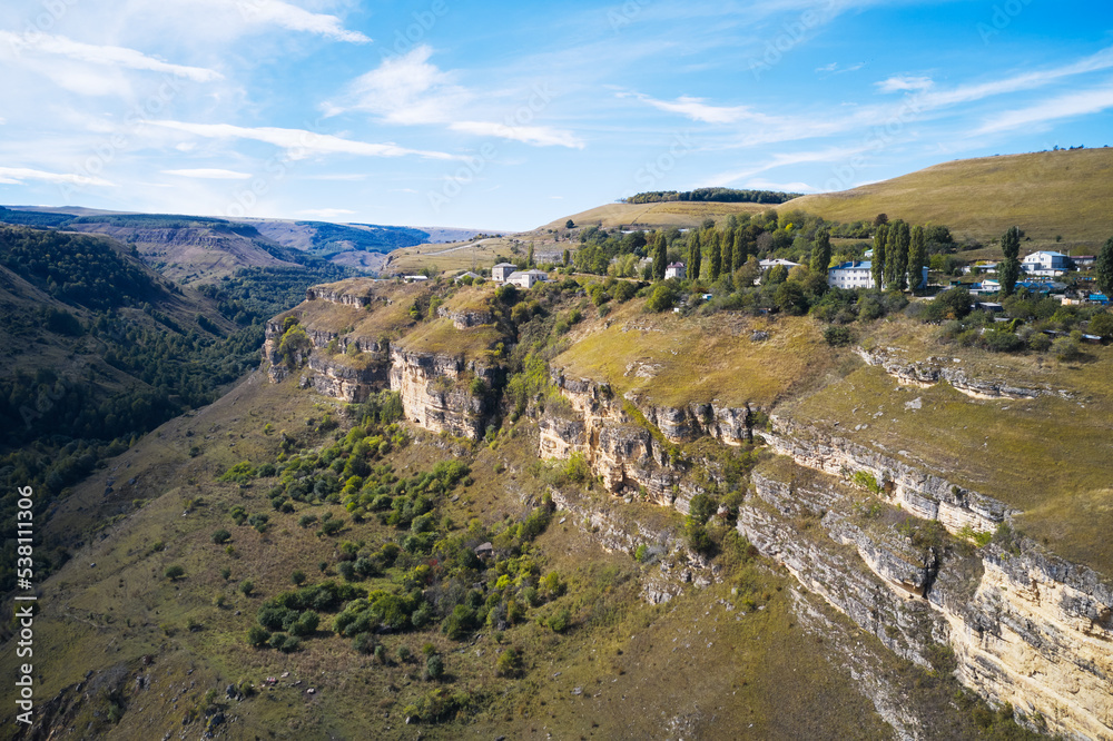 A mountain gorge with rocky slopes and a mountain village in the greenery above. Shooting from a drone.