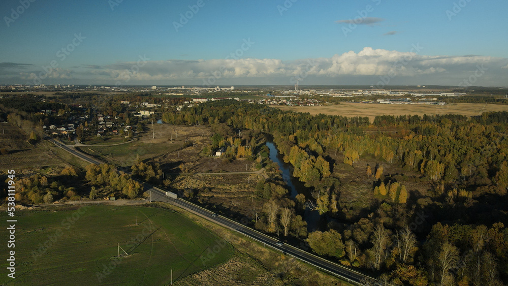 Agricultural fields. On the horizon you can see the settlement and the highway. Around the forest with colorful autumn leaves. Aerial photography.