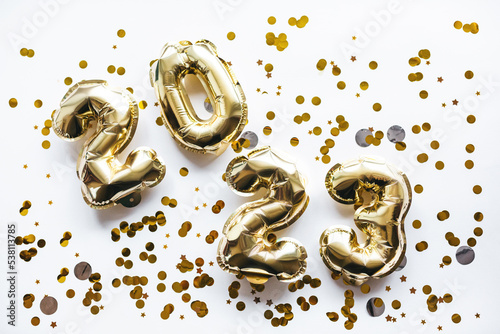 Carelessly scattered balloons made of gold foil in the form of the numbers 2023 with confetti on a white background. Celebrating Christmas, New Year and holiday concept. Flat position, top view.