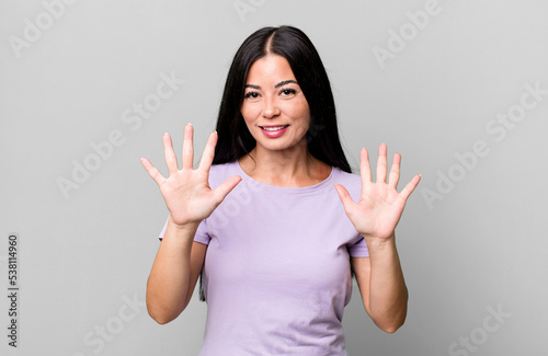 pretty latin woman smiling and looking friendly, showing number ten or tenth with hand forward, counting down photo