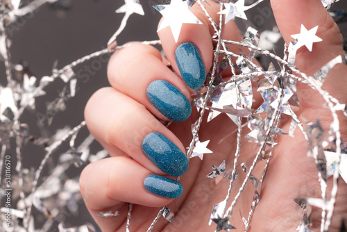 Female hand with beautiful holiday manicure - blue glitter nails with silver Christmas twisted wire with stars. Selective focus. Closeup view. Nail care concept