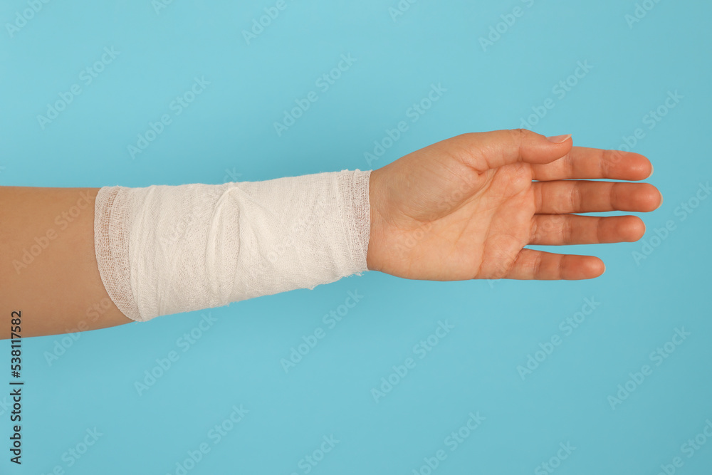 Woman with wrist wrapped in medical bandage on light blue background, closeup