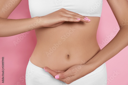 Woman in underwear holding something near her belly on pink background, closeup. Healthy stomach