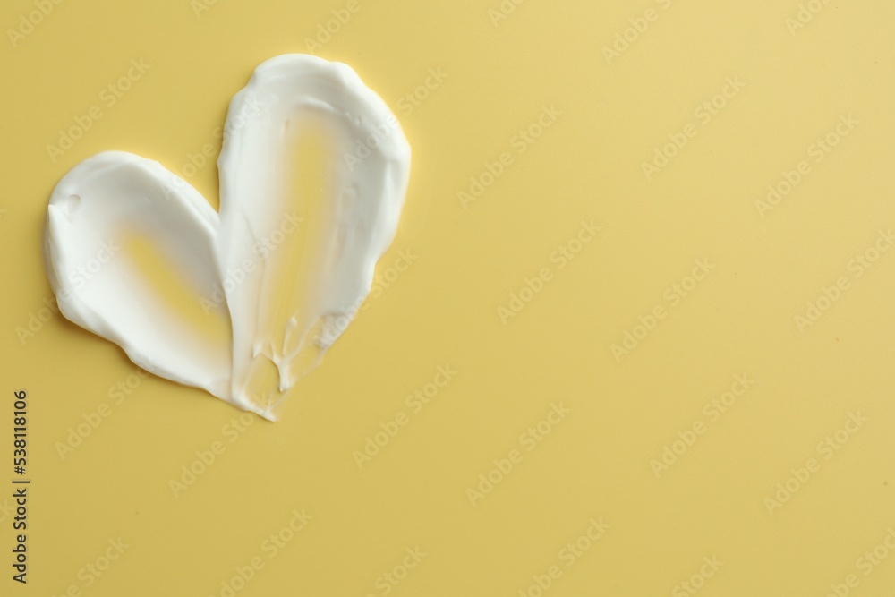 Samples of face cream in shape of heart on yellow background, top view. Space for text